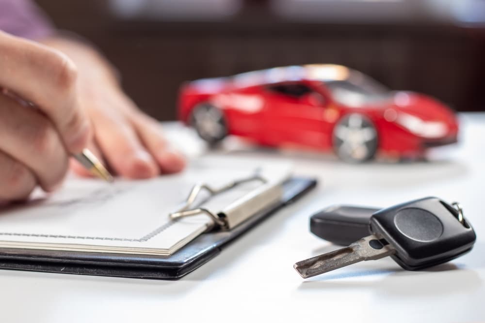 Signing an auto insurance application, with car keys and a model car on the desk